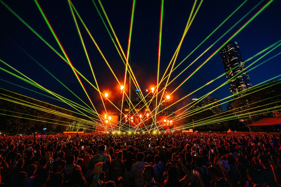 Green and yellow laser beams fan across a massive nighttime crowd at Lollapalooza, converging over the main stage.