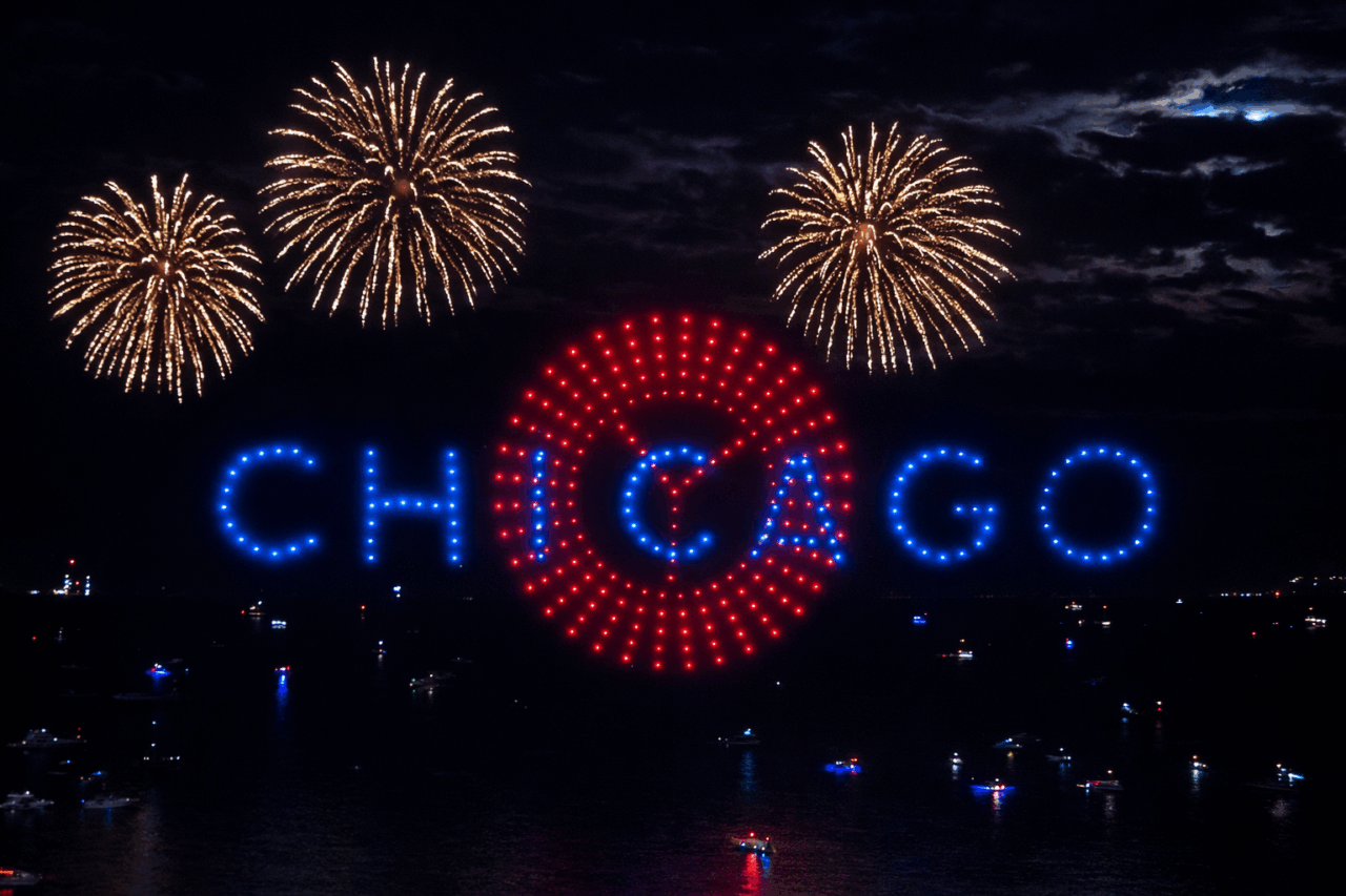 Drone formations in a nighttime sky over Grant Park create colorful patterns above Taste of Chicago, with city lights visible below.